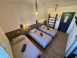 A hotel room with three beds, wooden floors, and a ladder leading to a door. - New Listing (Montenois)