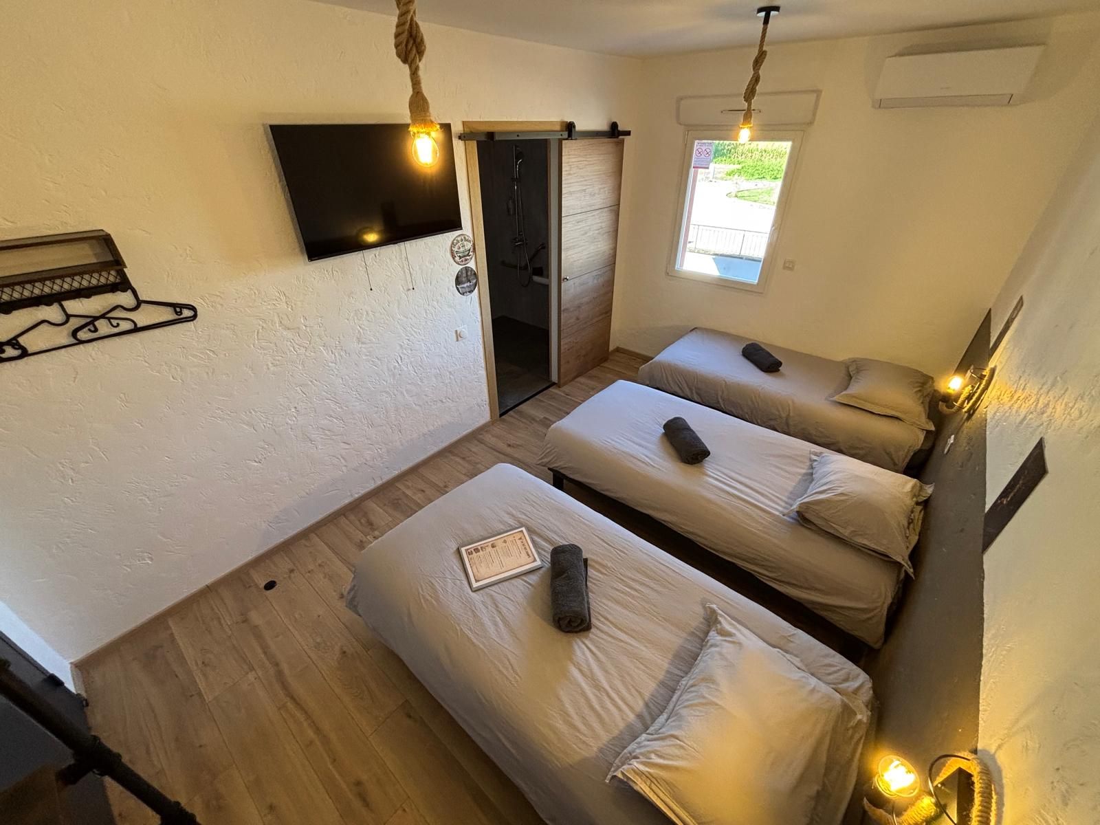 Une chambre avec trois lits, un téléviseur fixé au mur et une fenêtre donnant sur un beau paysage.