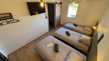 Une chambre avec trois lits, un téléviseur fixé au mur et une fenêtre donnant sur un beau paysage.