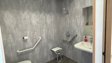 Une salle de bain moderne équipée de toilettes, de barres d’appui, d’une douche et d’un lavabo.