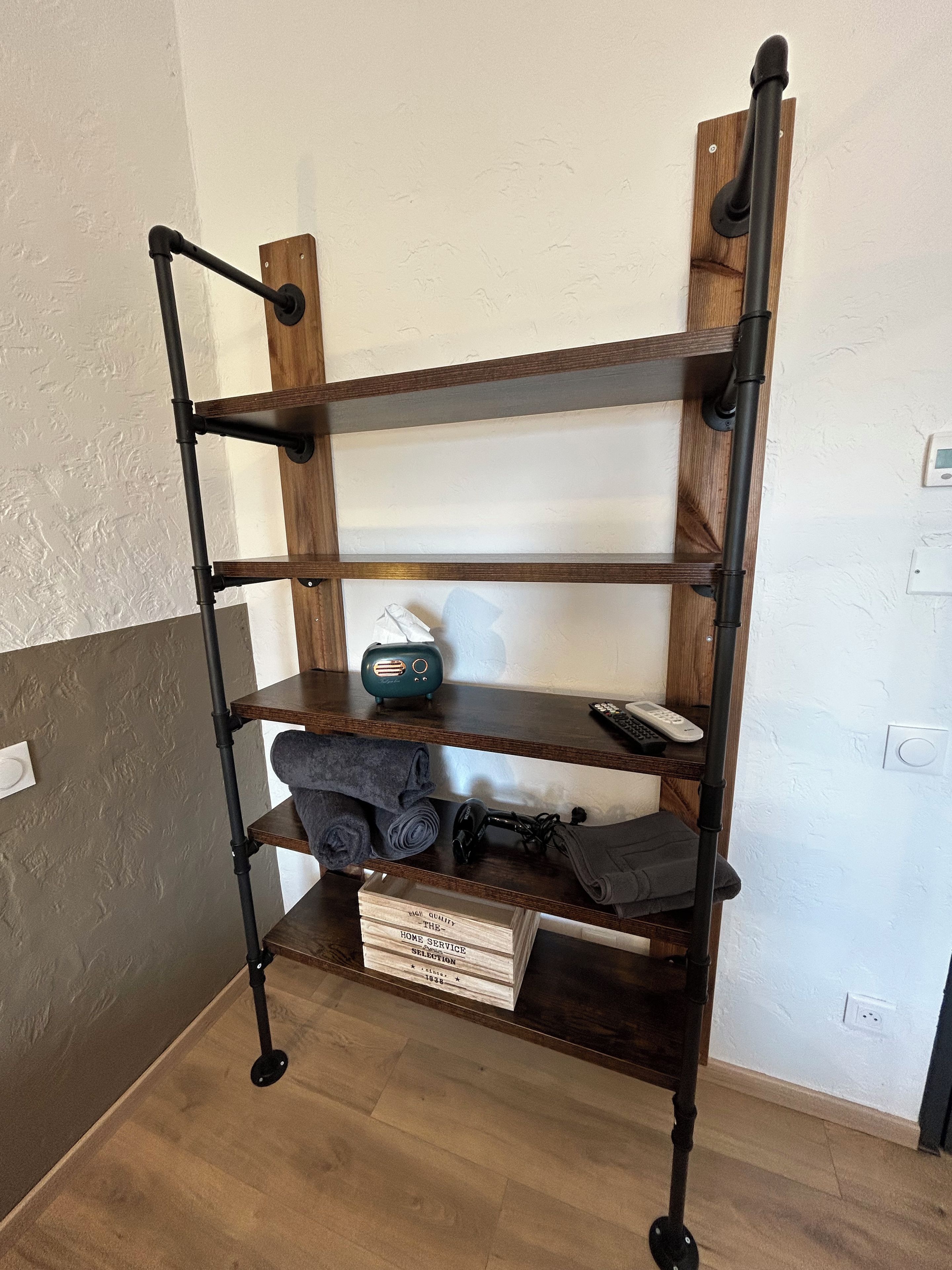 A wooden shelf unit with multiple shelves, a radio, and a box labeled 'HIGH QUALITY THE HOME SERVICE COLLECTION.'