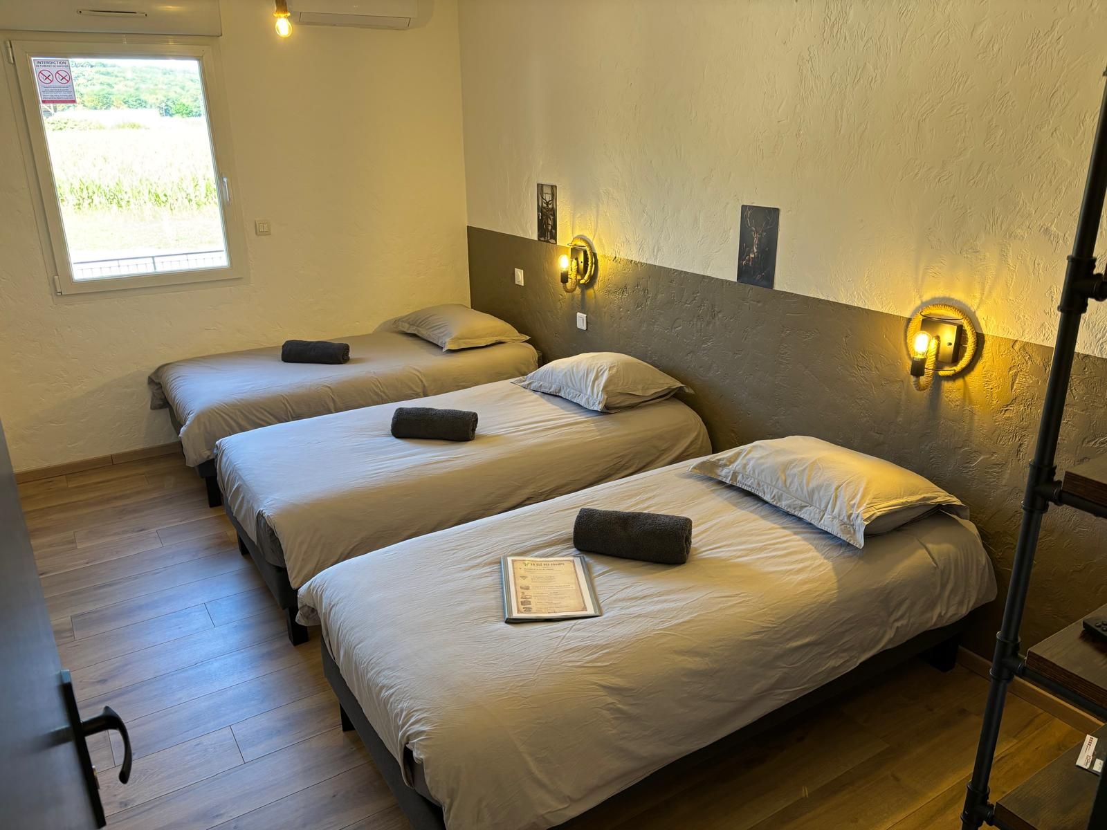 A hotel room with three beds, a window with a view, and a wall-mounted light fixture.