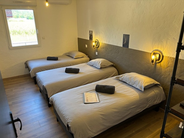 A hotel room with three beds, a window with a view, and a wall-mounted light fixture. - New Listing (Montenois)