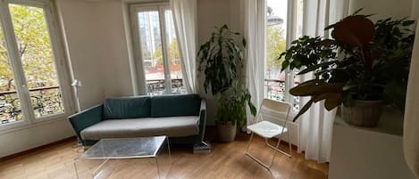 Una habitación con sofá, sillón, mesa y ventanas amplias.