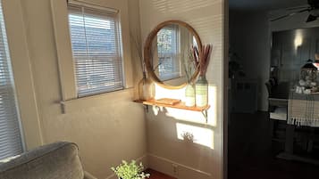 En stue med sofa, et lille bord med en plante, et spejl og et vindue med persienner.