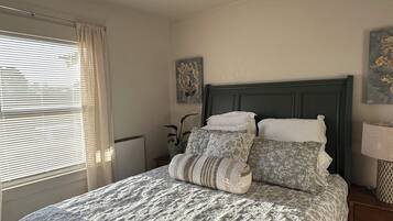 A bedroom with a bed, a nightstand, a lamp, a window with blinds, and a ceiling light.