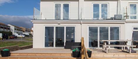 En moderne bygning i to etager med store skydedøre, en træterrasse og udendørs møbler.