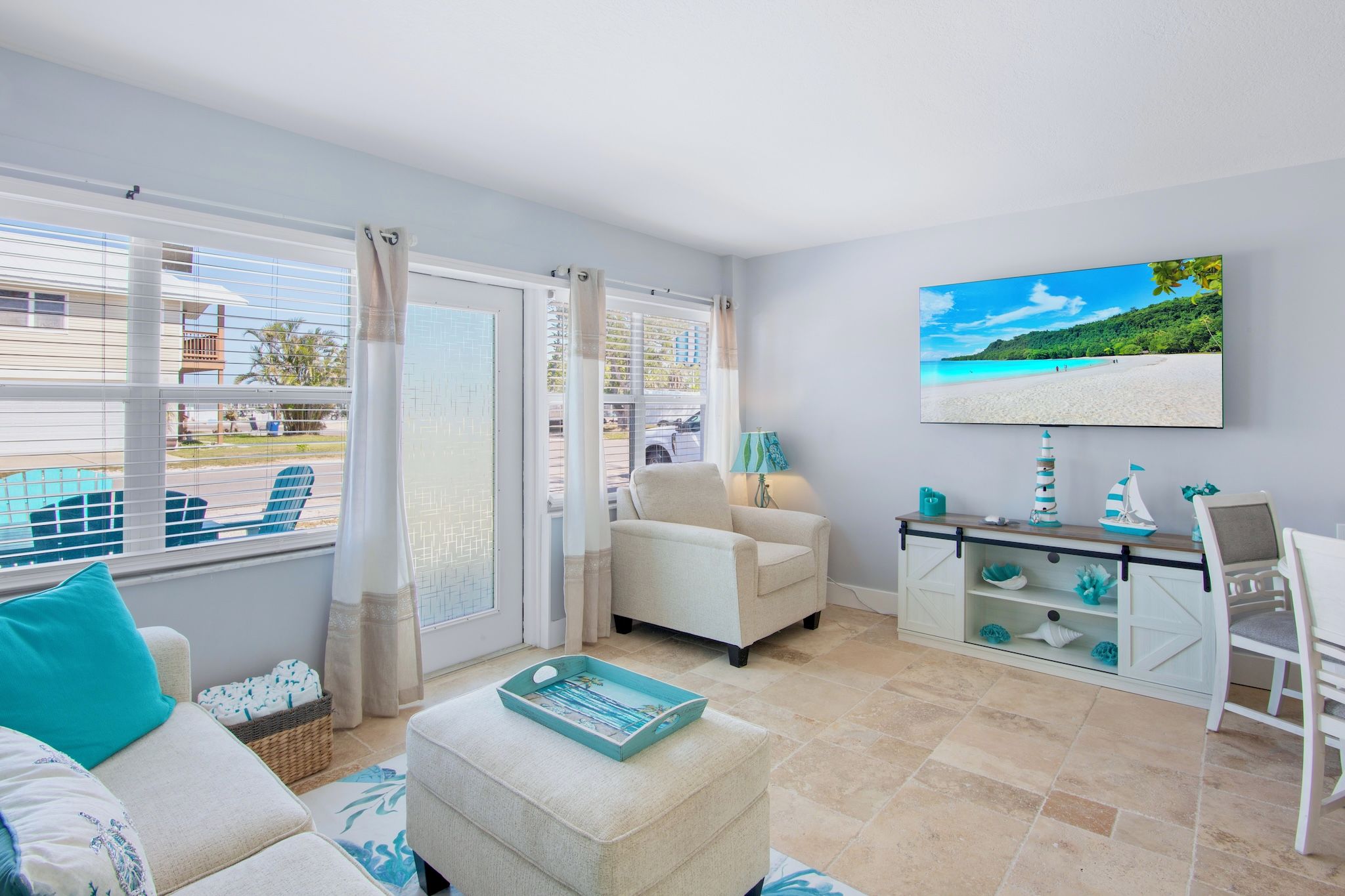 A living room with a view of the beach, a sofa, a chair, a coffee table, and a TV on the wall.