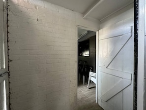 A hallway with white brick walls, a white door, and a partially visible room with a chair and table. - 4 bedroom House in Guildford! (Surrey)