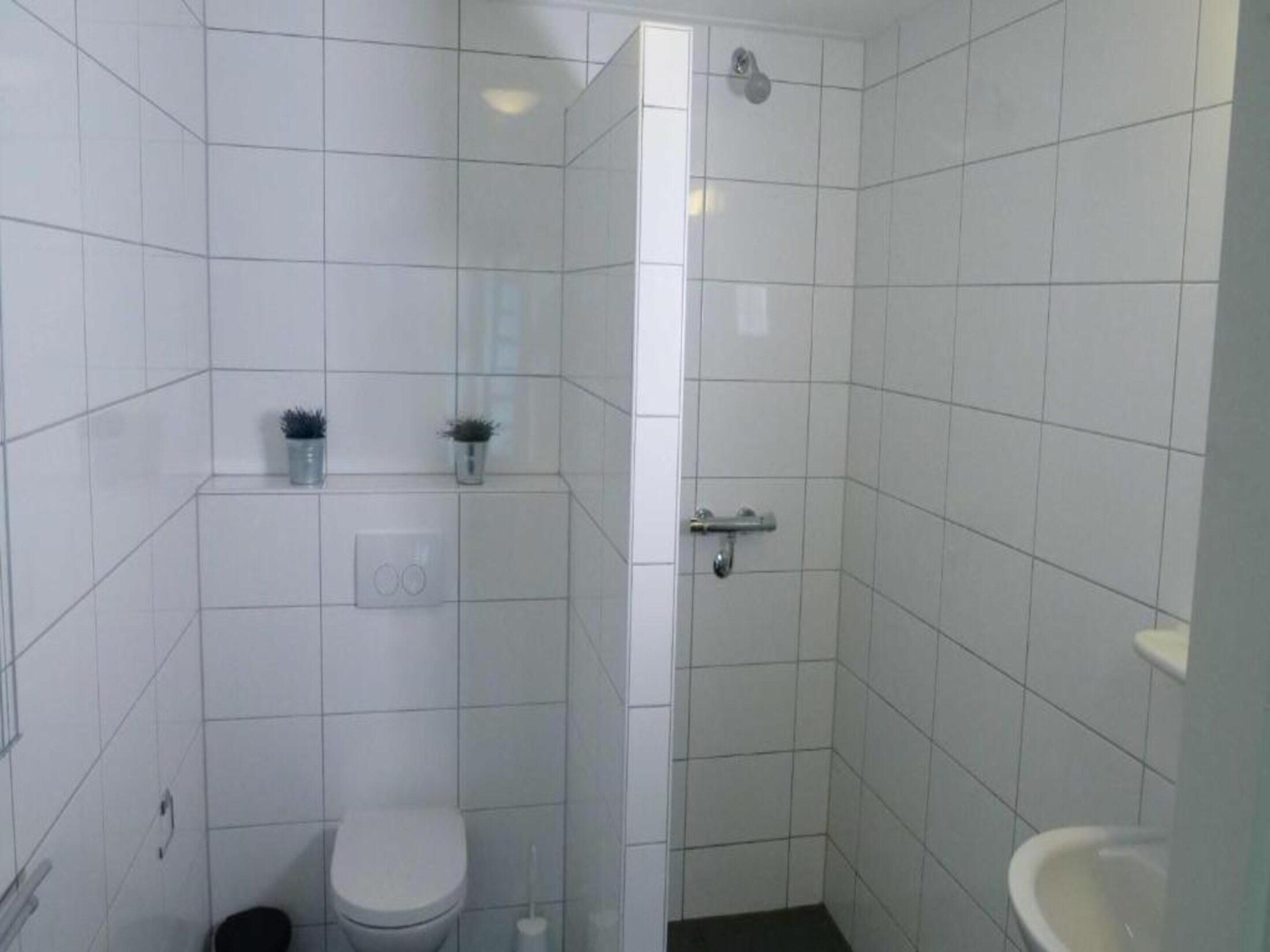 A small, tiled bathroom with a toilet, bidet, and a shower area.