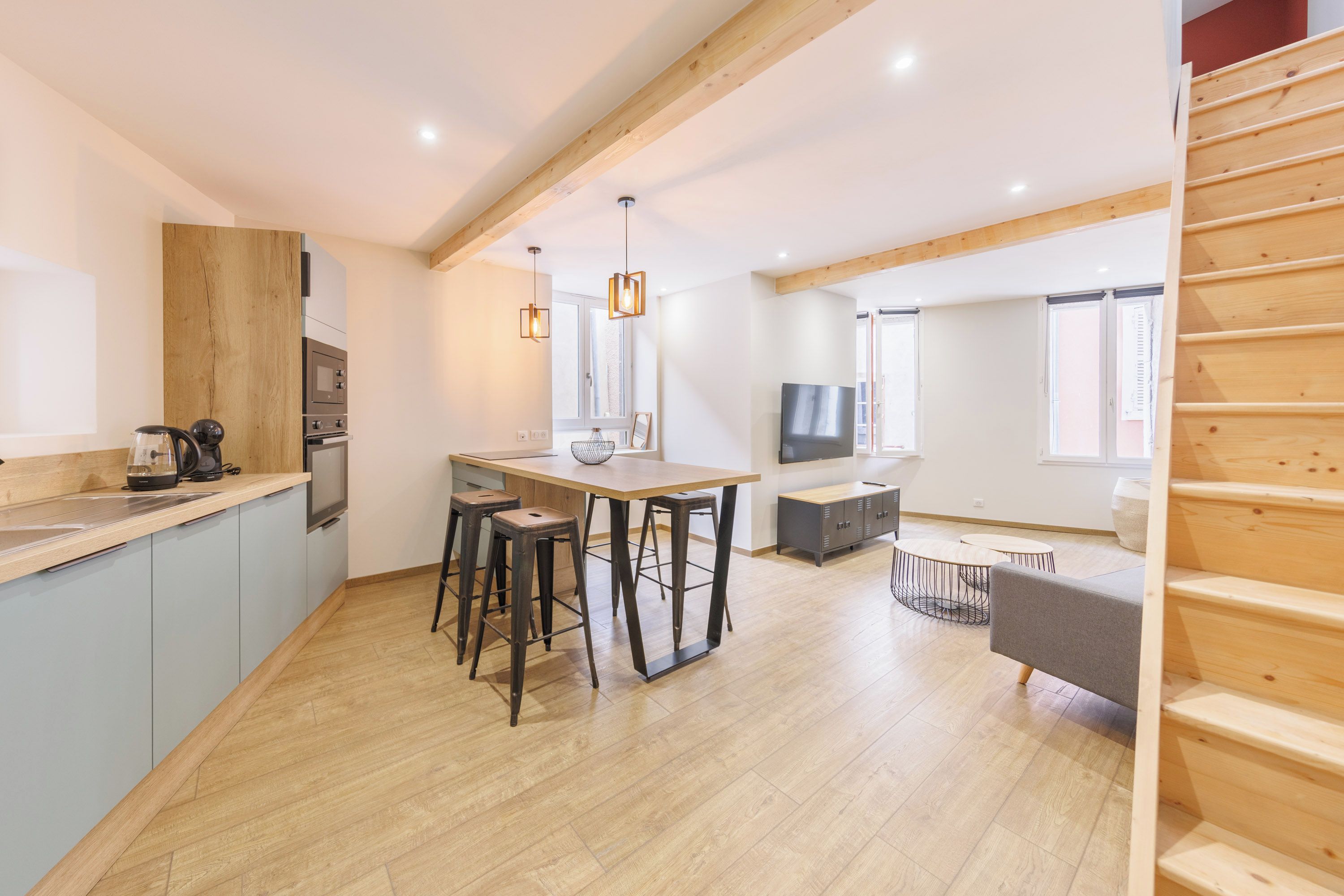 Una cocina moderna con una isla de madera, taburetes de bar, una mesa de comedor y un televisor.