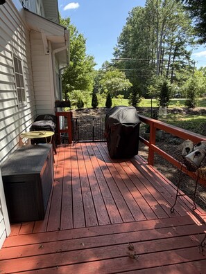 Een houten terras met buitenmeubilair, een overdekte barbecue en een metalen hek.