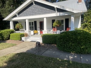 Een huis met twee verdiepingen, een veranda, een hond en verzorgde beplanting.