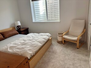 Ein Schlafzimmer mit Bett, Sessel, Nachttisch und einem Fenster mit Jalousien.