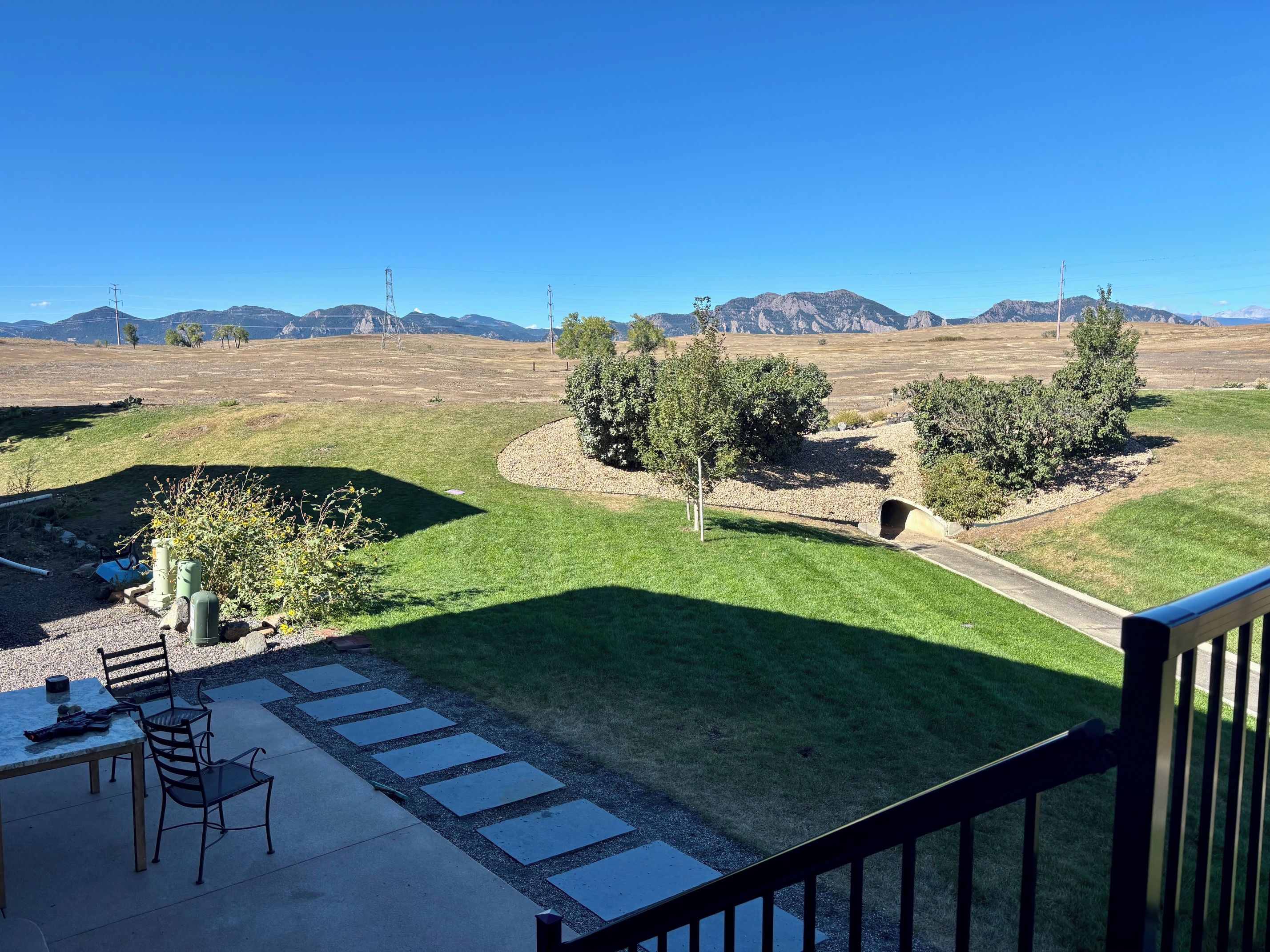 A patio with outdoor furniture, a stone pathway, and a view of a grassy field with trees and mountains in the distance.