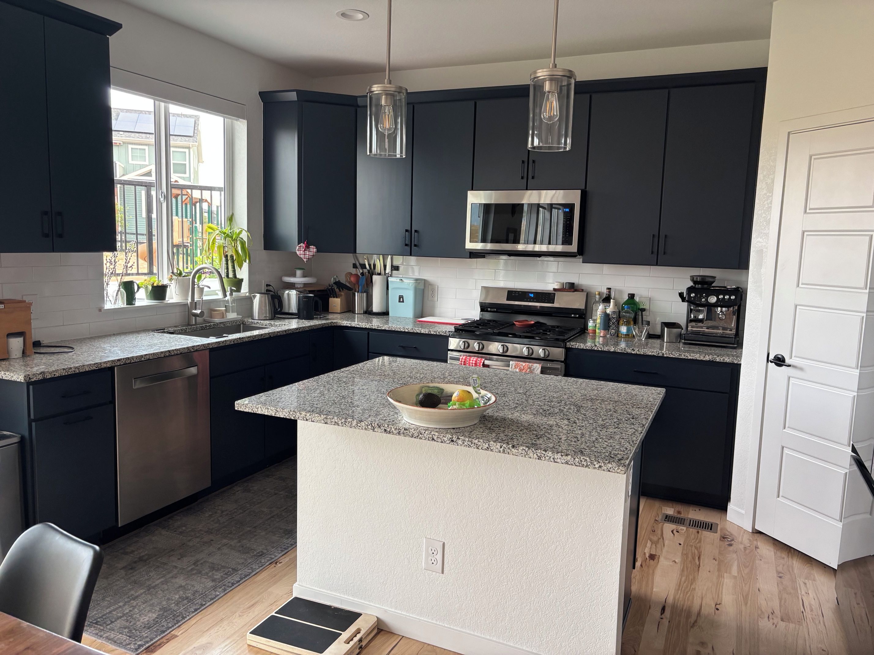A modern kitchen with dark cabinets, a central island, stainless steel appliances, and pendant lighting.