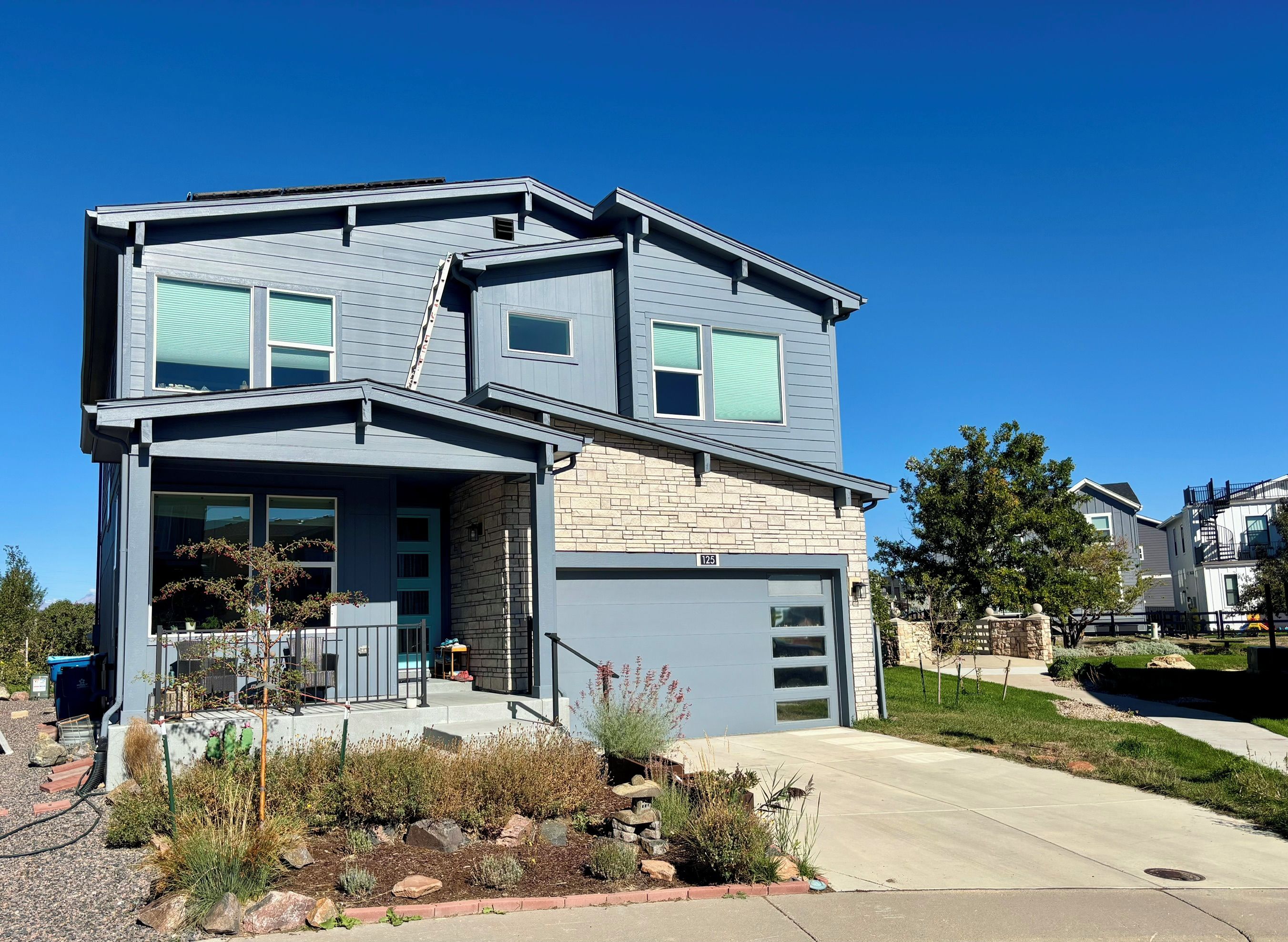 A modern two-story house with a garage, stone facade, and a well-maintained front yard.