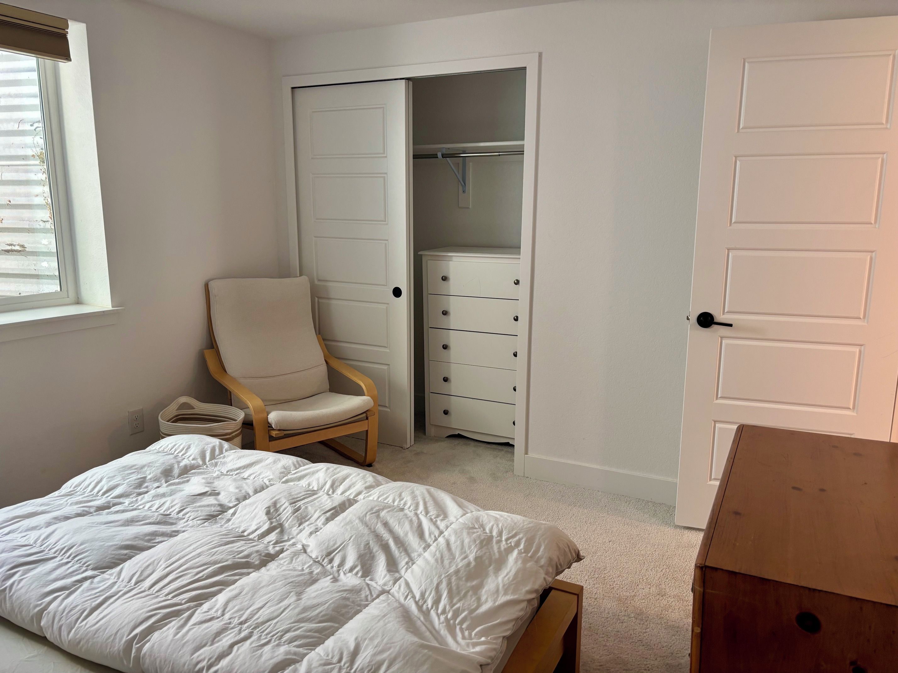 A bedroom with a bed, a chair, a wardrobe, and a door.