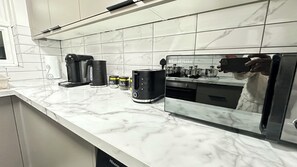 Una cocina con encimera de mármol, cafetera, tostadora y refrigerador.