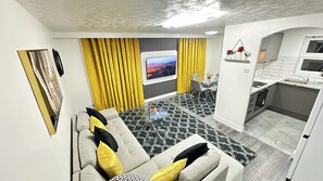 Una sala moderna con un sofá, un televisor de pantalla plana y un comedor con una mesa de vidrio.