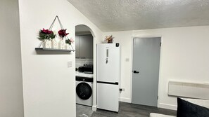 Una cocina compacta con lavadora, un refrigerador blanco y una puerta que da a otra habitación.