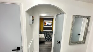 Un couloir avec une porte, un miroir et un téléviseur dans une pièce.
