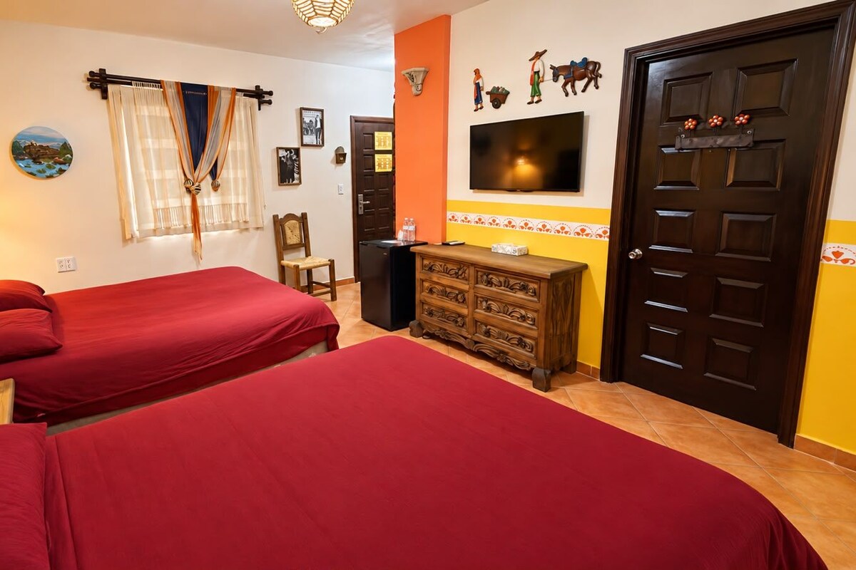 A hotel room with two beds, a wooden dresser, a TV, and a door with a decorative handle.