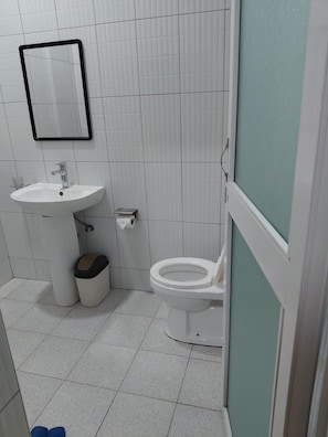 Un baño con lavamanos, inodoro, espejo y cubo de basura.