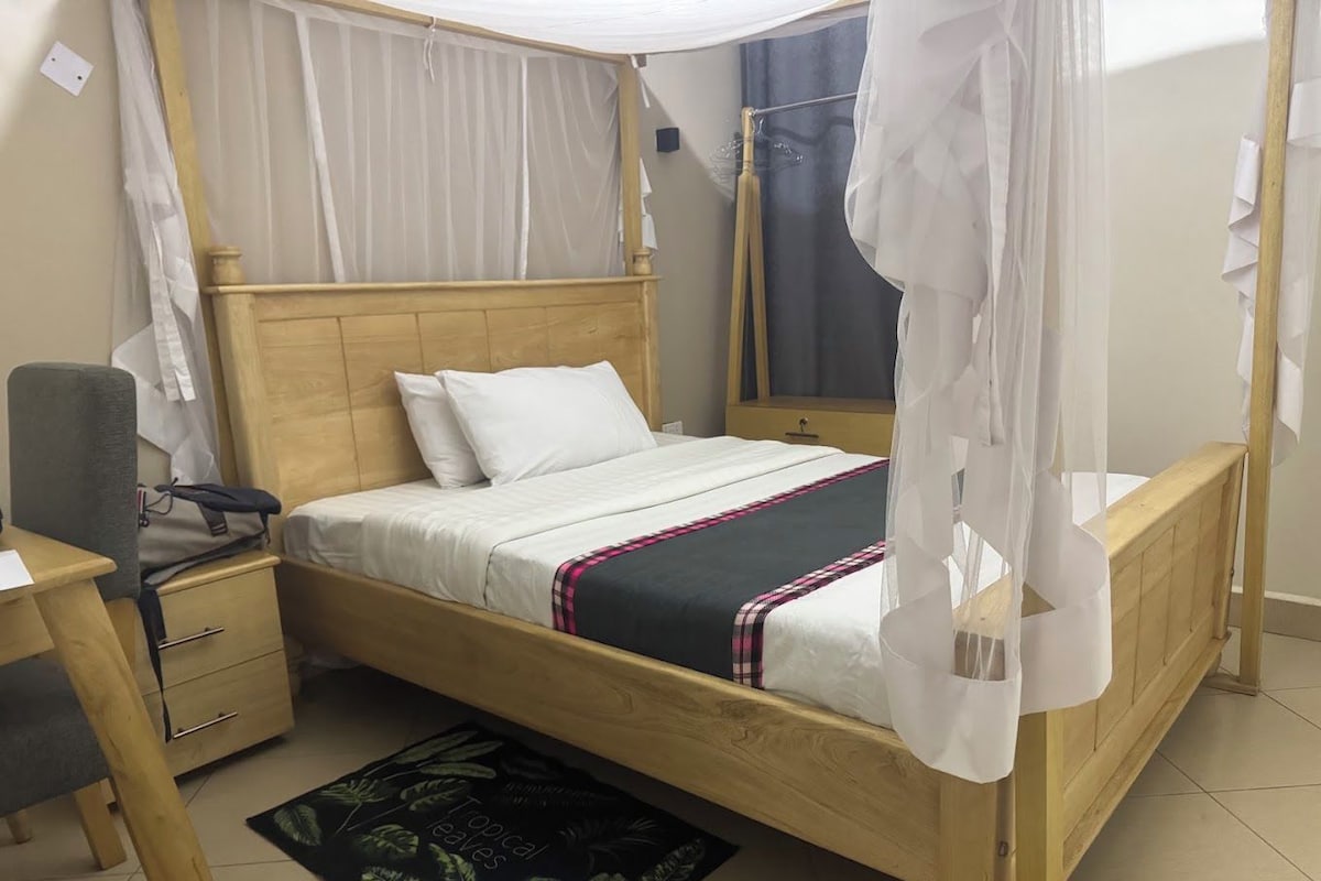 Una cama individual con dosel, una mesita de noche, una silla y un pequeño escritorio con su propia silla.