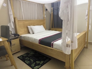 Una cama individual con dosel, una mesita de noche, una silla y un pequeño escritorio con su propia silla.