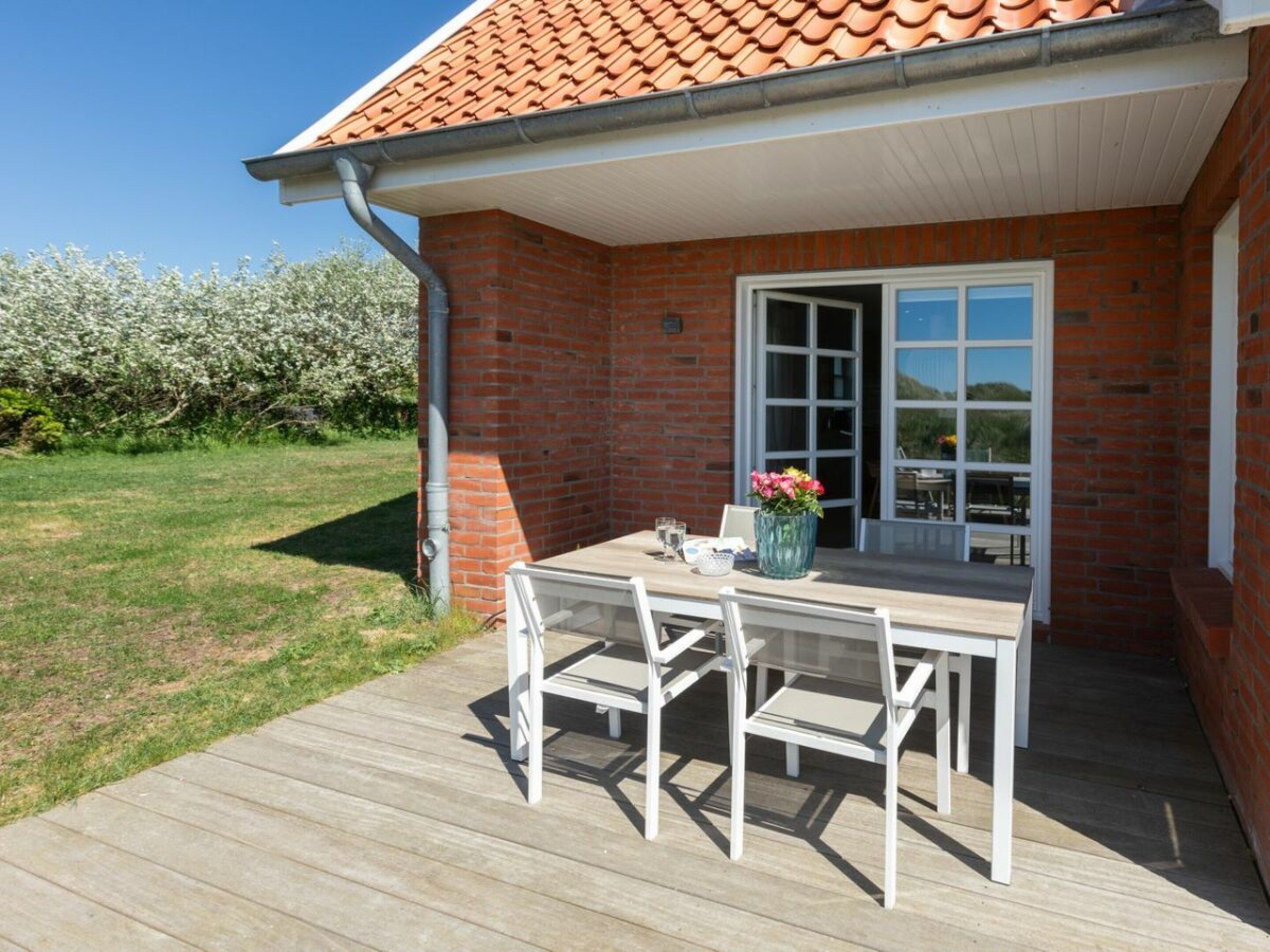 A patio with a table and chairs, a brick building with a tiled roof, and a clear sky.
