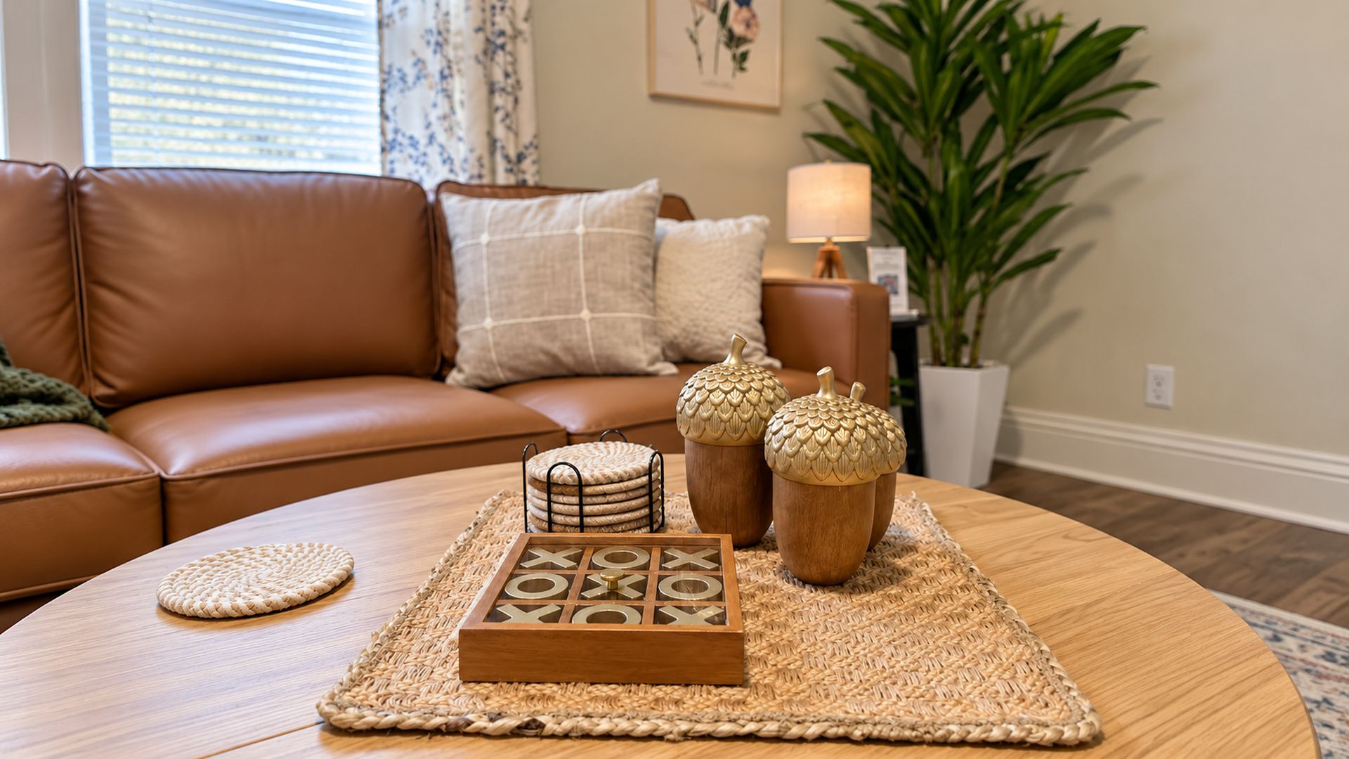 A living room with a brown leather sofa, a round coffee table with woven placemats, decorative wooden items, and a potted plant.