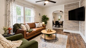 A living room with a brown leather sofa, a round coffee table, and a dining area with a wooden table and chairs. - Comfortable Home Base | Near ND, IUSB & Hospitals (Mishawaka)