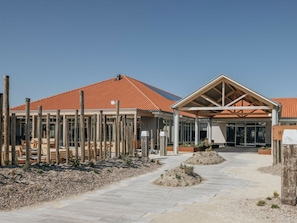 A building with a red-tiled roof, a covered entrance area, and a paved walkway leading to the entrance.
