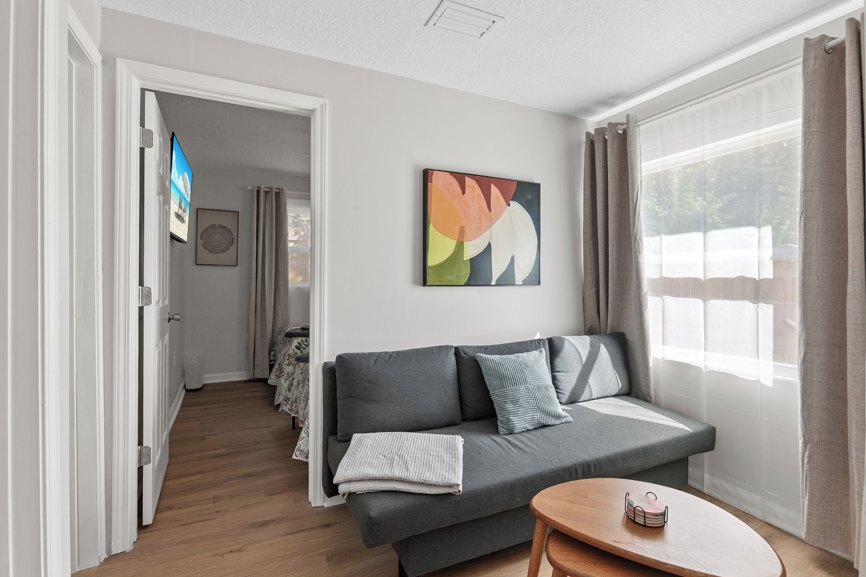 A modern living room with a grey sofa, a small wooden table, and a colorful abstract painting on the wall.