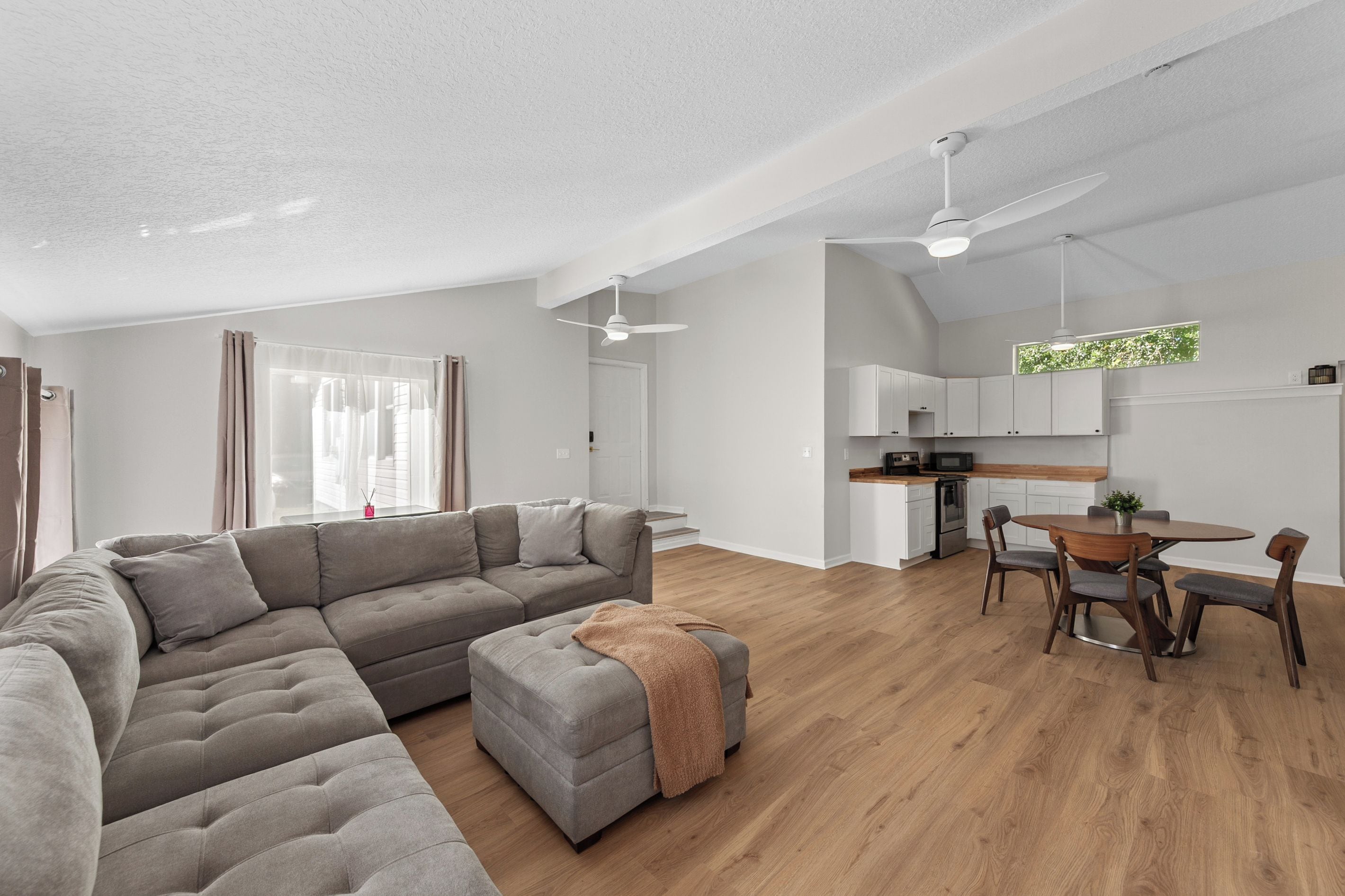 A modern living space with a sectional sofa, a dining area with a round table and chairs, and a kitchen with white cabinets and a wooden countertop.
