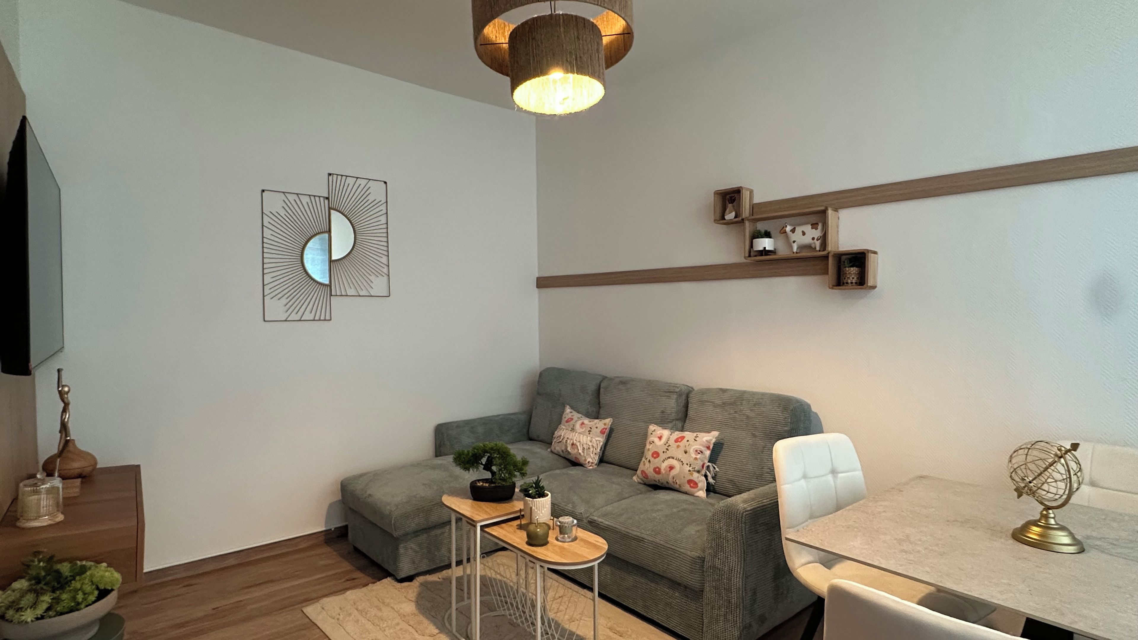 A modern living room with a grey sofa, a small table with a plant, a wooden shelf with decorative items, and a globe on a table.