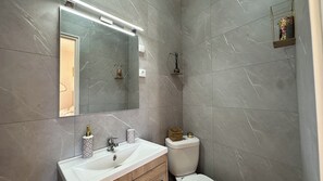 Ein Badezimmer mit einem weißen Waschbecken, einem Spiegel, einer Toilette und einer Duschkabine.