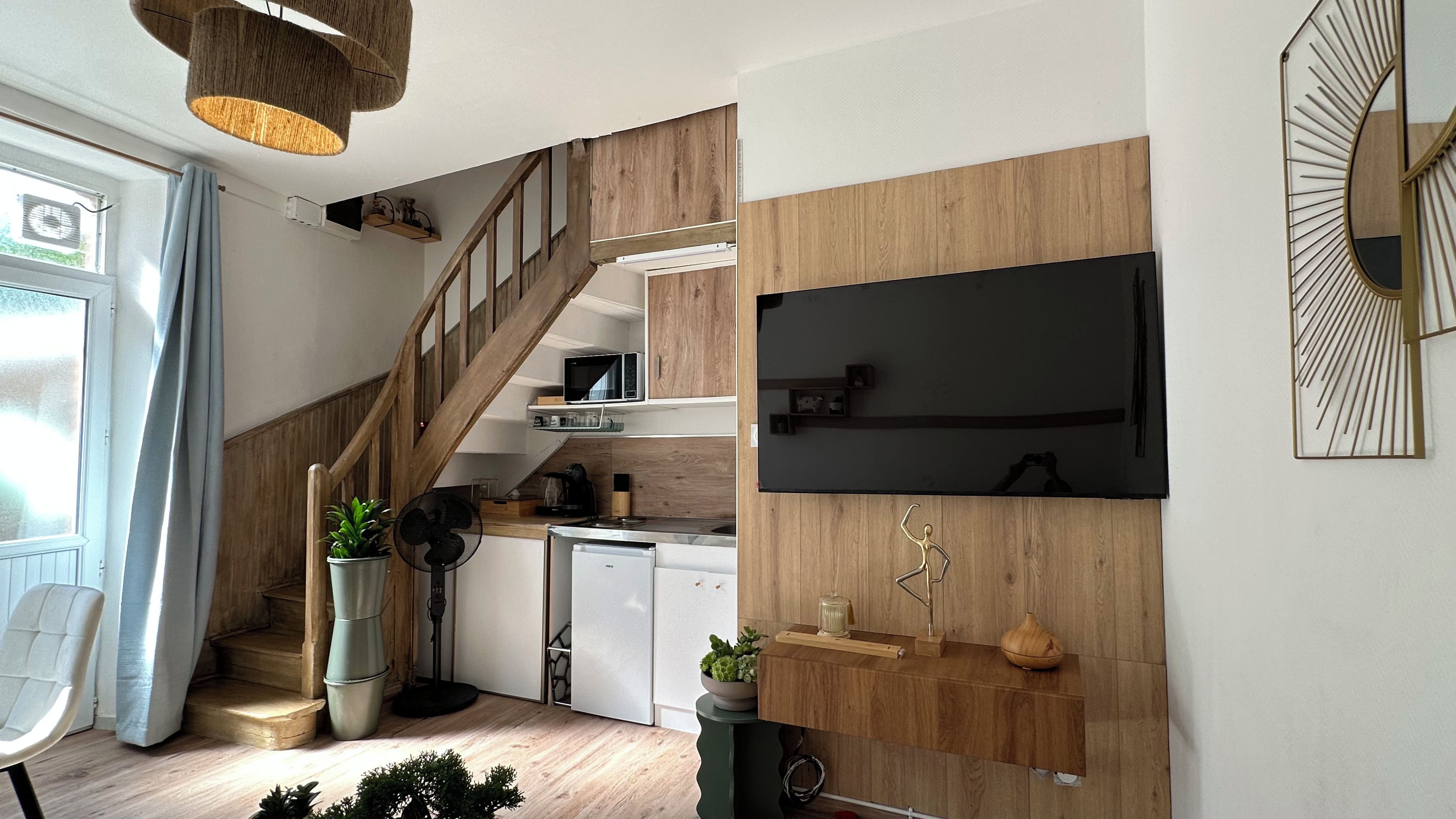 Une cuisine moderne avec un escalier en bois, des appareils électroménagers intégrés et un téléviseur à écran plat fixé au mur.