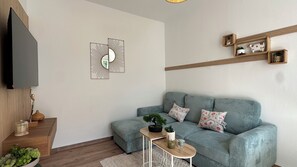 Ein modernes Wohnzimmer mit einem grauen Sofa, einem kleinen Beistelltisch und einem wandmontierten Flachbildfernseher.