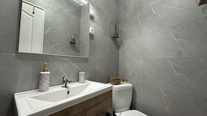 Une salle de bain avec un lavabo blanc, un miroir, des toilettes et un espace douche.