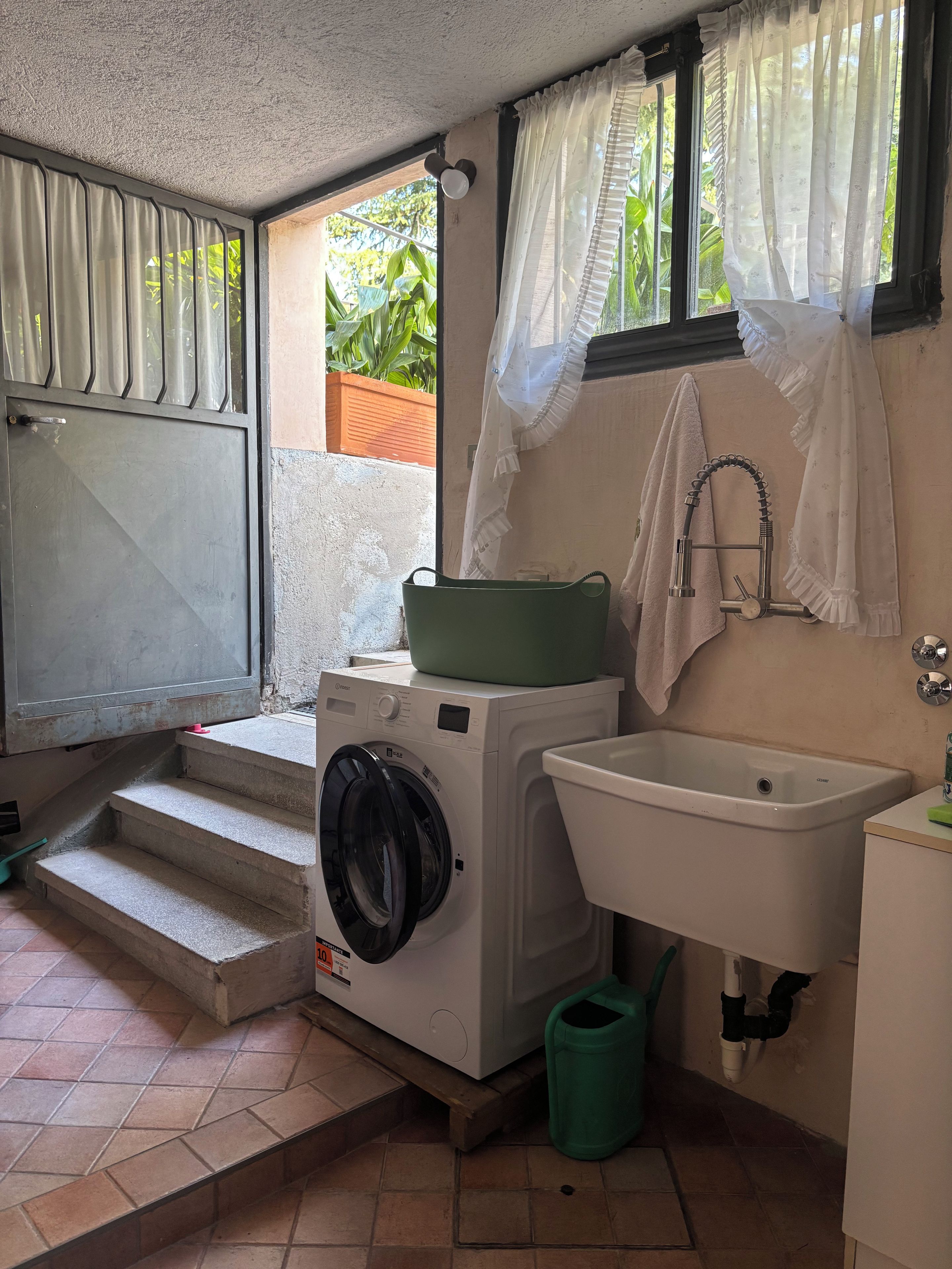 A compact laundry area with a washing machine, a sink, and a green trash bin.