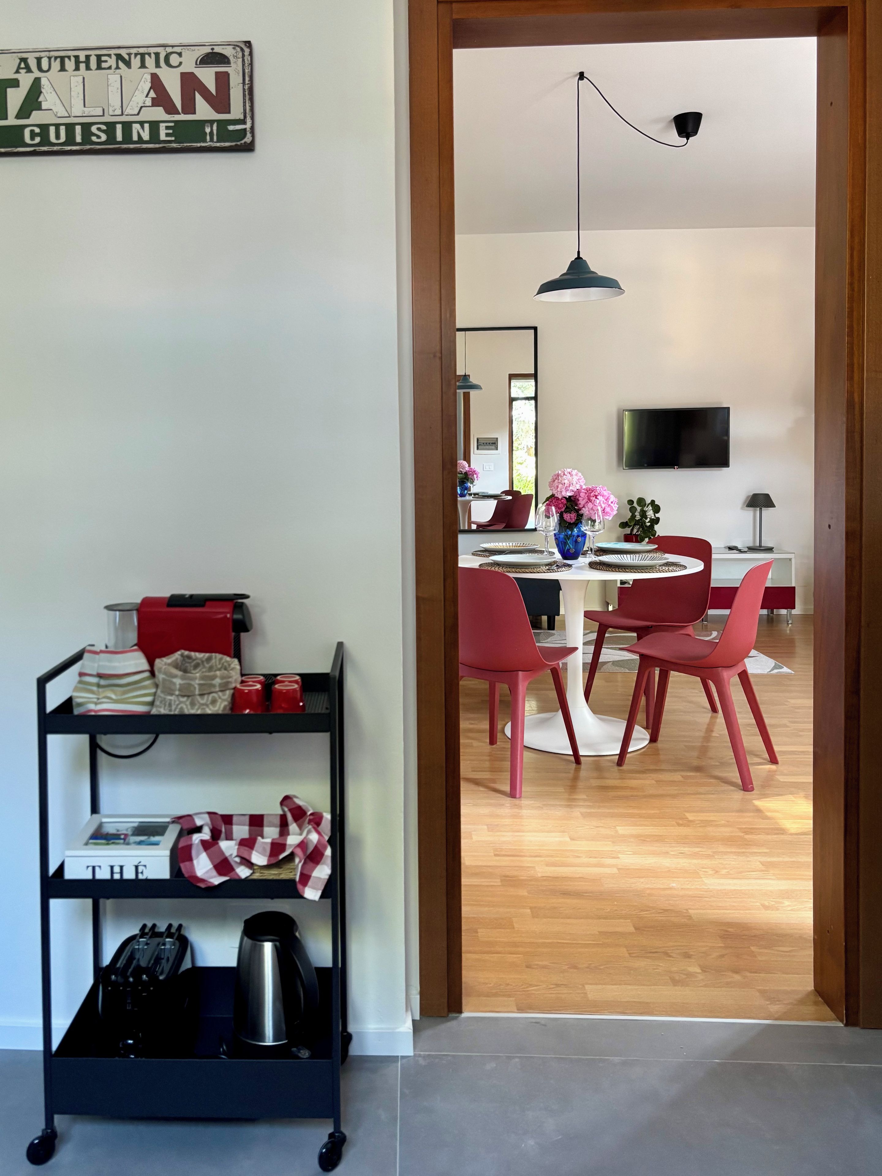 A modern kitchen with a black metal cart, red chairs, and a dining table.