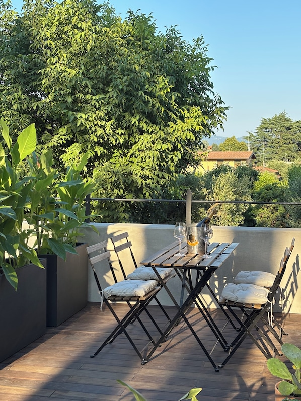 Un patio al aire libre con una mesa y sillas de madera, rodeado de follaje y vistas al cielo.