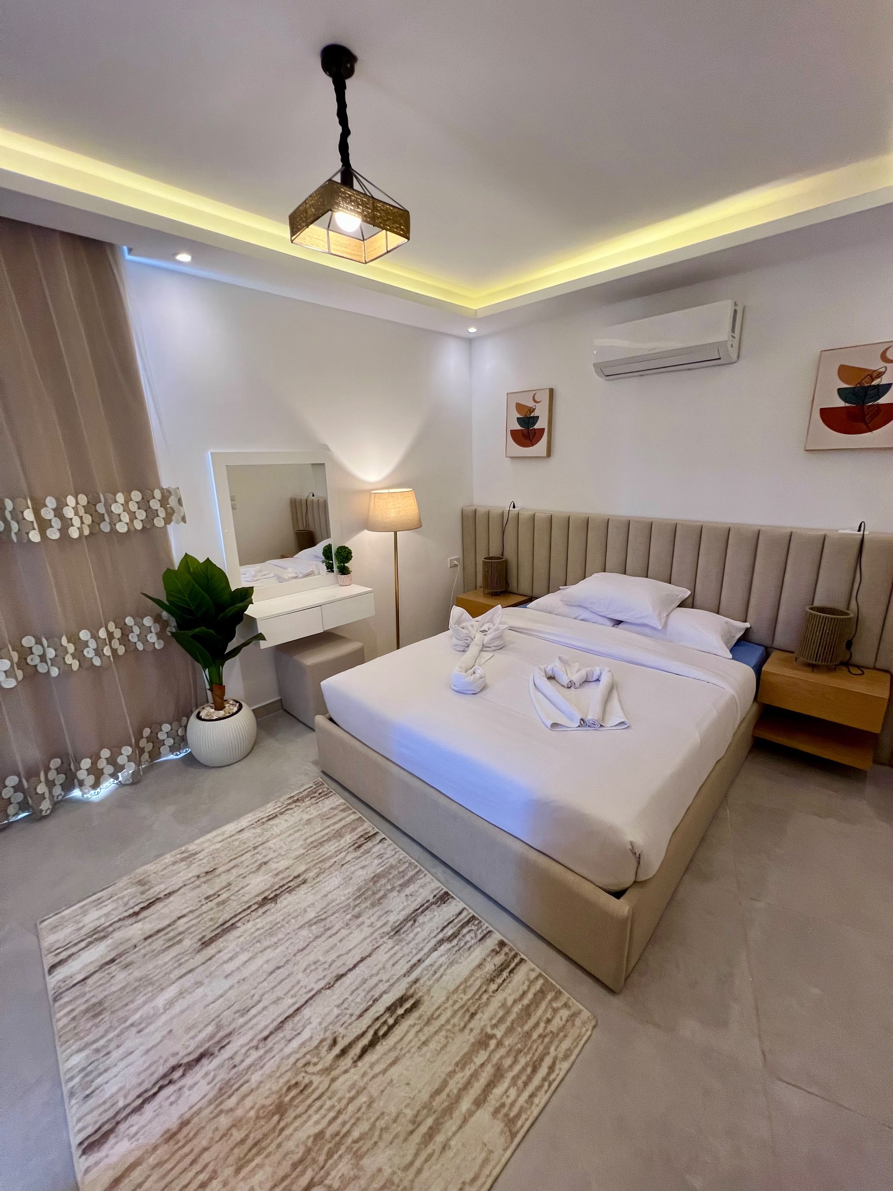 Moderni hotellihuone, jossa on suuri sänky, yöpöydät, peili ja kattovalaisin.