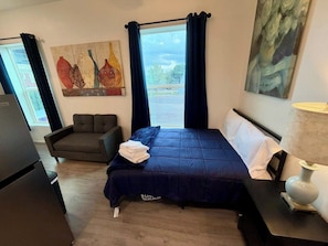 Quarto de hotel com cama, sofá, quadro e janela com cortinas.