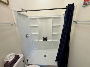 Área de chuveiro com porta de vidro, porta-toalhas e prateleira com artigos de higiene pessoal.