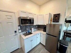 A compact kitchen with white cabinets, a stainless steel refrigerator, a microwave, and a sink. - Historic Broad St Apt 3 in Upton’s Confectionery (Globe)