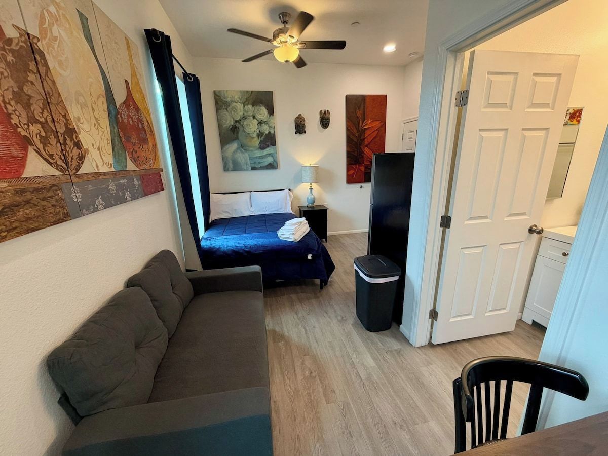 Ein kleines Zimmer mit einem Bett, einer Couch, einem Fernseher und einem Deckenventilator.