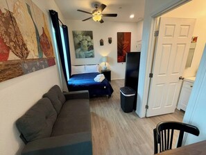 A compact room with a bed, a sofa, a TV, and a ceiling fan. - Historic Broad St Apt 3 in Upton’s Confectionery (Globe)